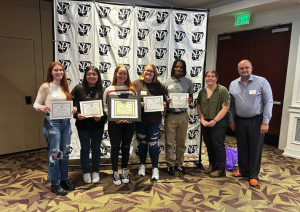 UCA Scroll students standing in front of banner holding their ACMA awards