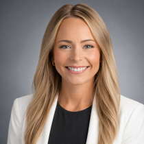 A polished professional headshot portrait of a smiling woman set against a seamless studio backdrop.